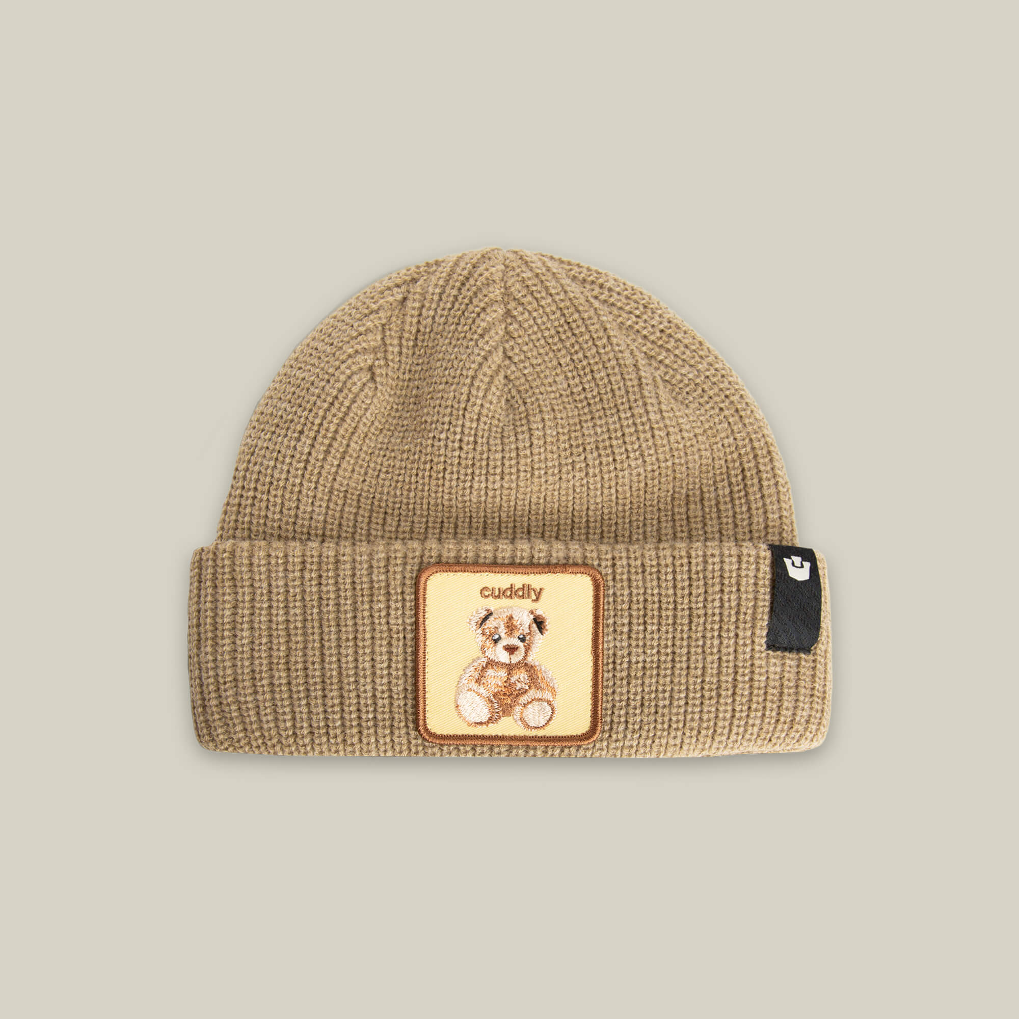 The Cuddly Beanie Mini by Goorin Bros. is a tan kids’ knit beanie with a folded brim, a teddy bear patch reading "cuddly," and a small black side tag.