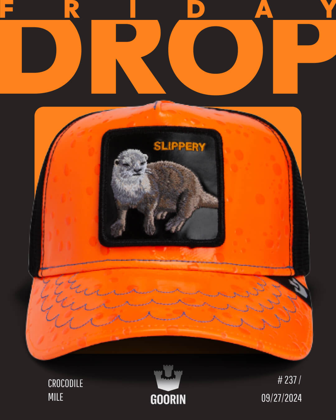 Bright orange trucker hat with an embroidered otter patch and the word SLIPPERY, set against a black background with bold orange text reading FRIDAY DROP—an eye-catching pick for fans of bold hat designs.