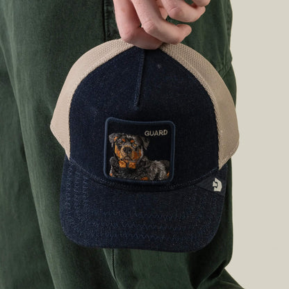 A person holds the Goorin Bros. Denim Guard snapback baseball cap in navy and beige, featuring a patch with an embroidered dog and the word “GUARD.”.