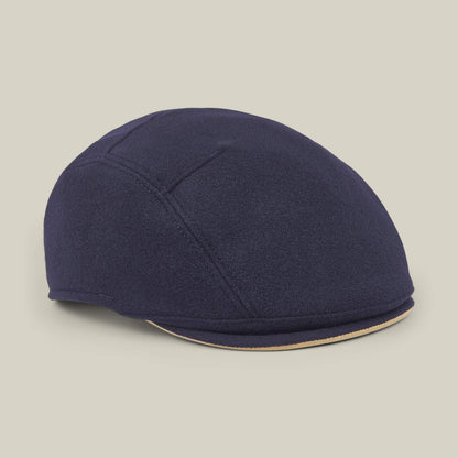 The Cornerstone flat cap by Goorin Bros. is a navy blue wool accessory featuring visible stitching details, handmade in New Jersey and displayed on a neutral background. This cap showcases a rounded crown and a short brim.