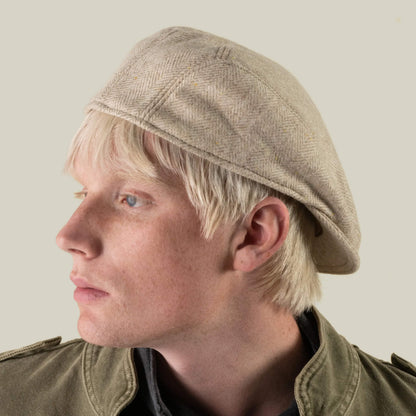 A person with light blond hair wears the Iris Fields flat cap by Goorin Bros.—a chalk cream headwear piece, hand-cut in the USA from 100% wool—as they look to the left. They are dressed in a green jacket against a plain background.