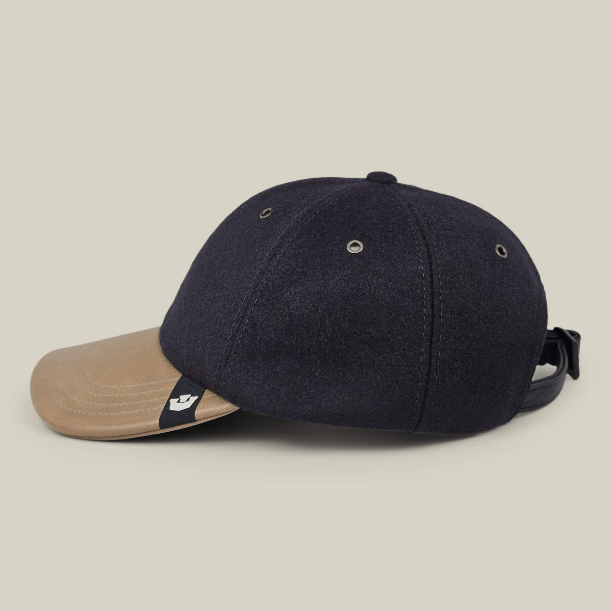 The Bixby cap by Goorin Bros. is a handmade, two-tone baseball cap crafted in New Jersey, showcasing a dark navy crown and a tan curved brim. It features metal eyelets and an adjustable strap at the back, displayed against a plain light background.