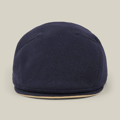 The Cornerstone flat cap by Goorin Bros.—a navy blue wool design, handmade in New Jersey with a round crown and short, curved brim—is photographed against a plain beige background.