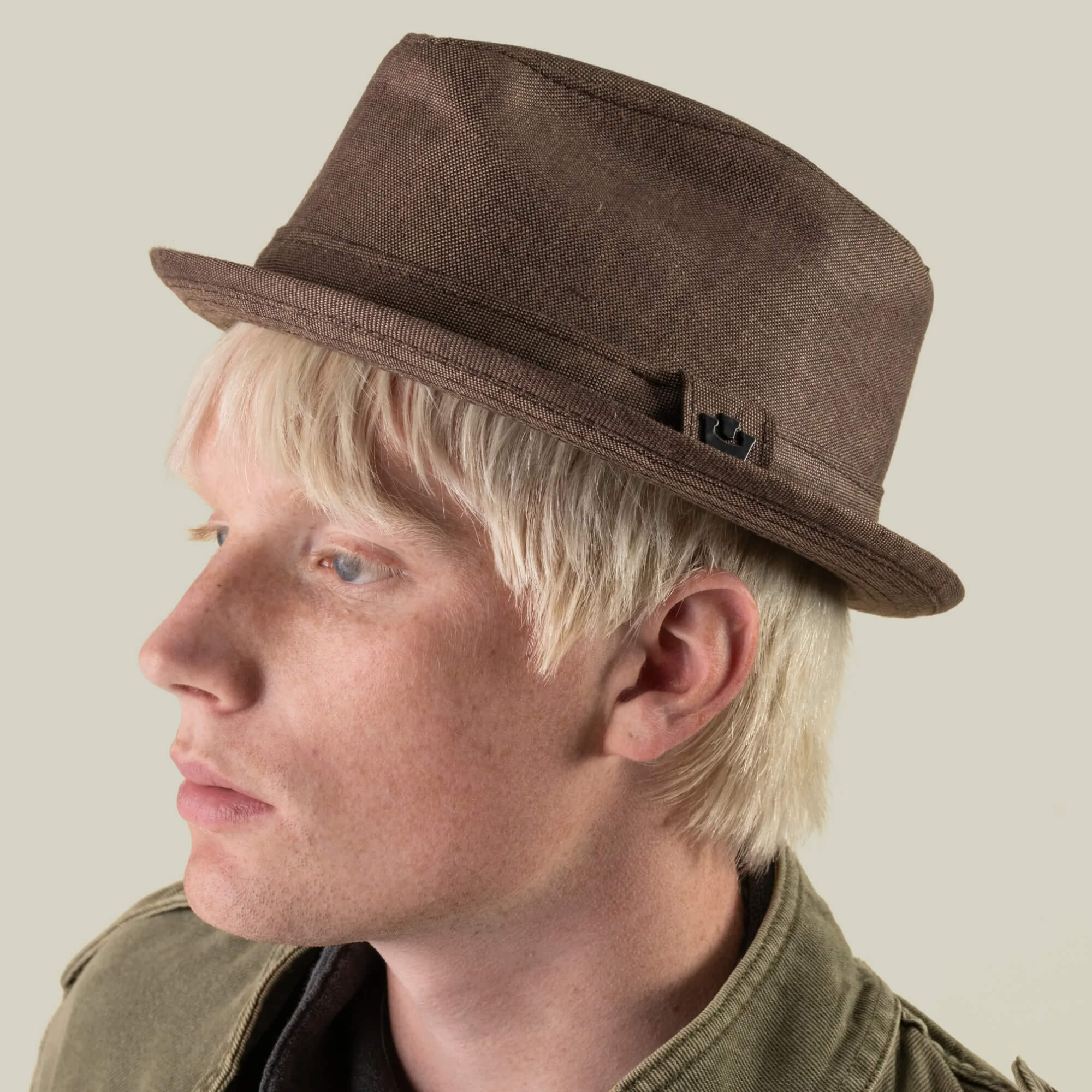 A person with light blonde hair, wearing the Goorin Bros. Charlie Pants and a brown fedora hat—hand-cut in the USA—paired with an olive green jacket, is viewed from the side against a plain background.