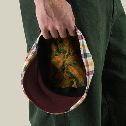 A person wearing green pants holds an upside-down Goorin Bros. Point Lobos cap—a handmade in USA 6 Panel Ivy style—showing its yellow and green patterned interior crafted from a breathable cotton blend.