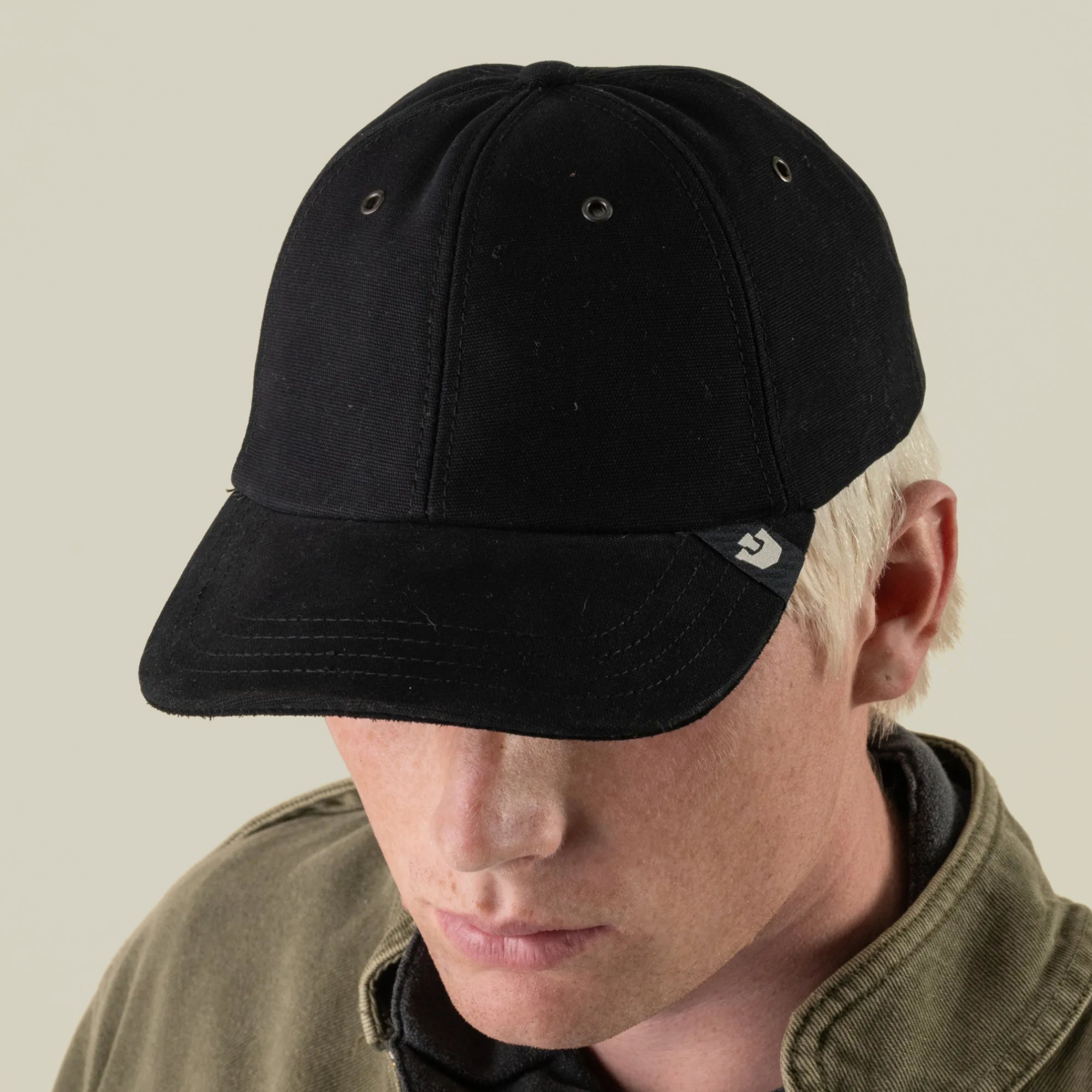 A person with light hair, wearing the Goorin Bros. Mineral Road mixed-material black baseball cap and a khaki jacket, is facing downward against a plain background.