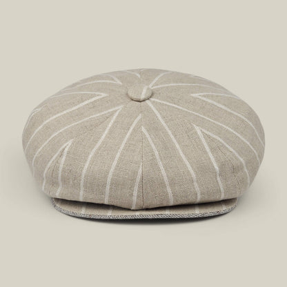 The Rincon Park by Goorin Bros. is a beige linen blend newsboy cap with white pinstripes, featuring a classic Gatsby silhouette with a button on top and a short, curved brim. Each cap is hand cut and sewn, and it is displayed against a neutral background.