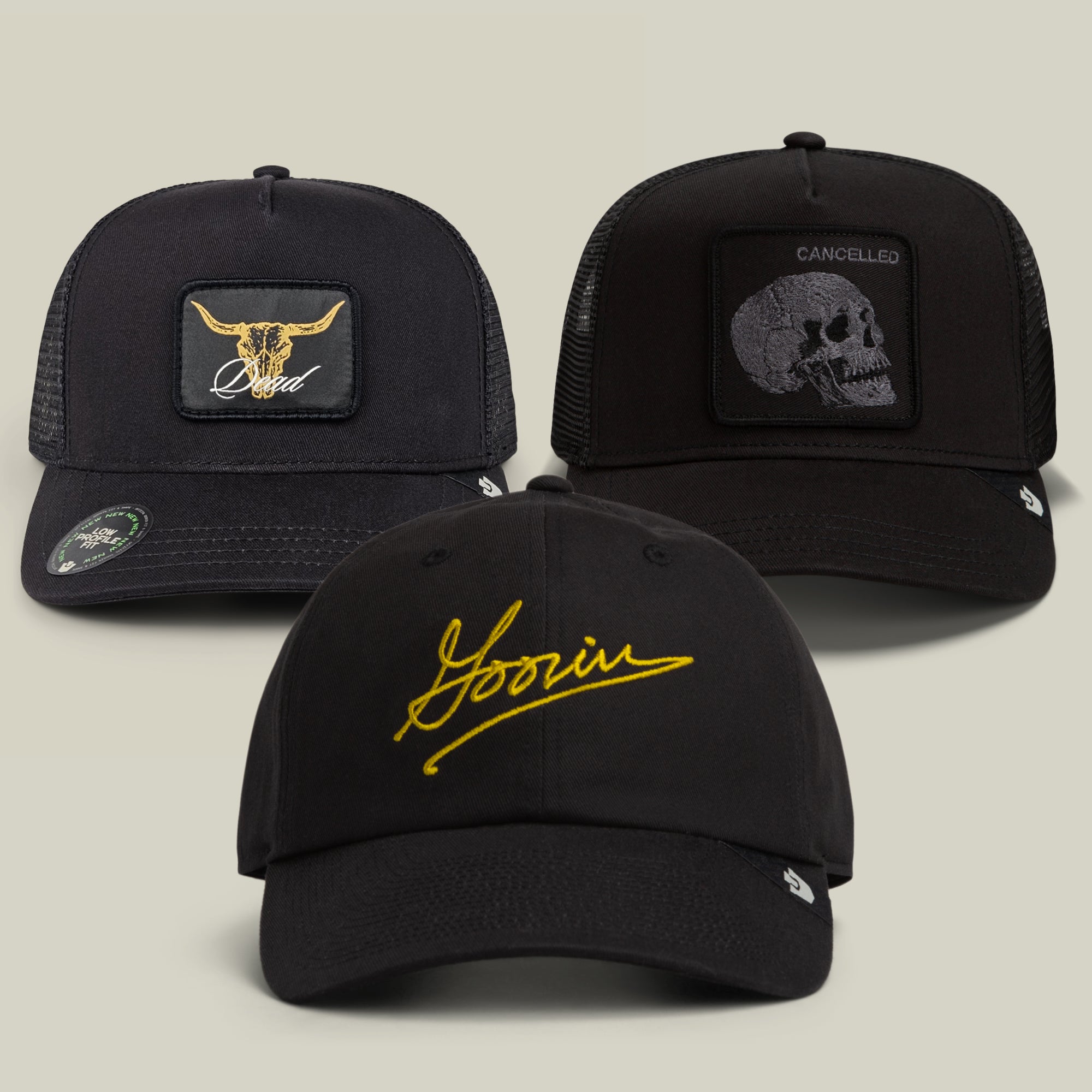 The Goorin Bros. All Black Every Shape Bundle features three black hats: one with a striking gold longhorn design, another with “Goorin” embroidered in yellow script, and a third adorned with a skull beneath the word “CANCELLED.”.
