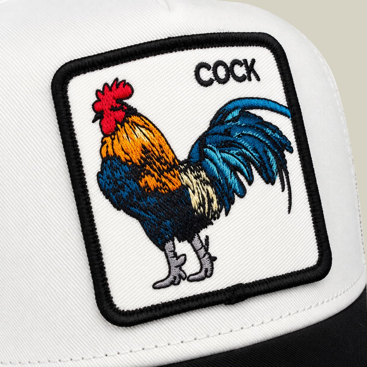 The Goorin Bros. Suede Colorful Rooster trucker hat features a white front panel with a colorful embroidered rooster patch and black text, paired with black mesh back panels. Close-up studio shot of the snapback cap's distinctive animal graphic design.