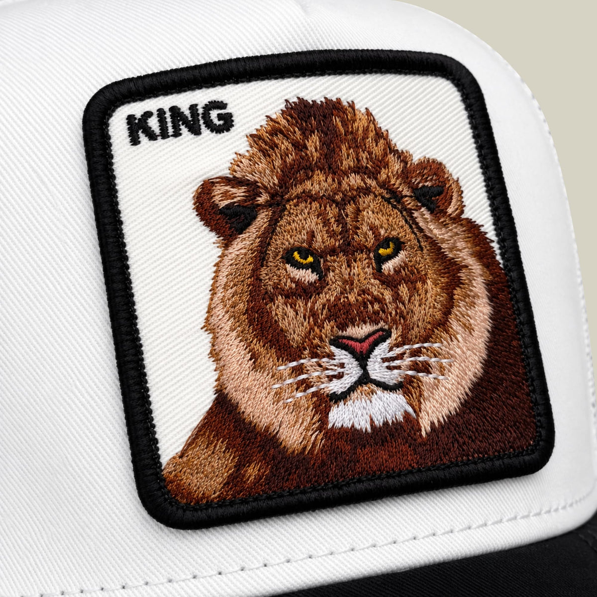 The Goorin Bros. Suede King trucker hat features a white front panel and black mesh back with an embroidered lion patch displaying golden eyes and the word "KING" above it.
