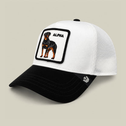 The Suede Alpha trucker hat by Goorin Bros features a white mesh back and black suede front with an embroidered rottweiler patch and alpha text on the crown, displayed on a neutral background.