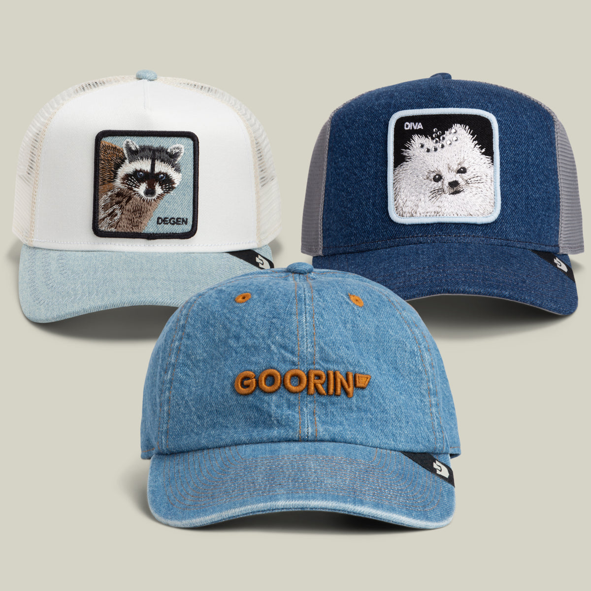 The Goorin Bros. Mom Jeans Bundle includes three caps: one white cap with a raccoon patch, one blue cap with a dog patch, and a light blue denim dad cap featuring bold orange GOORIN text. All feature visible black-and-white Goorin logo tags.
