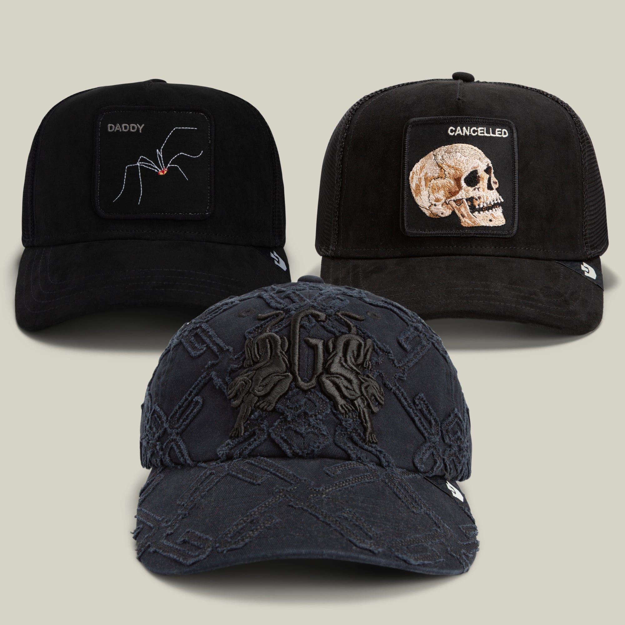 Three black baseball caps from the Goorin Bros. “Your Favorite Bundle” are displayed: one featuring a Bold Suede Spider and “DADDY” lettering, another with a Bold Suede Skull and “CANCELLED,” and a front cap embossed with an FBD pattern and stylized design.