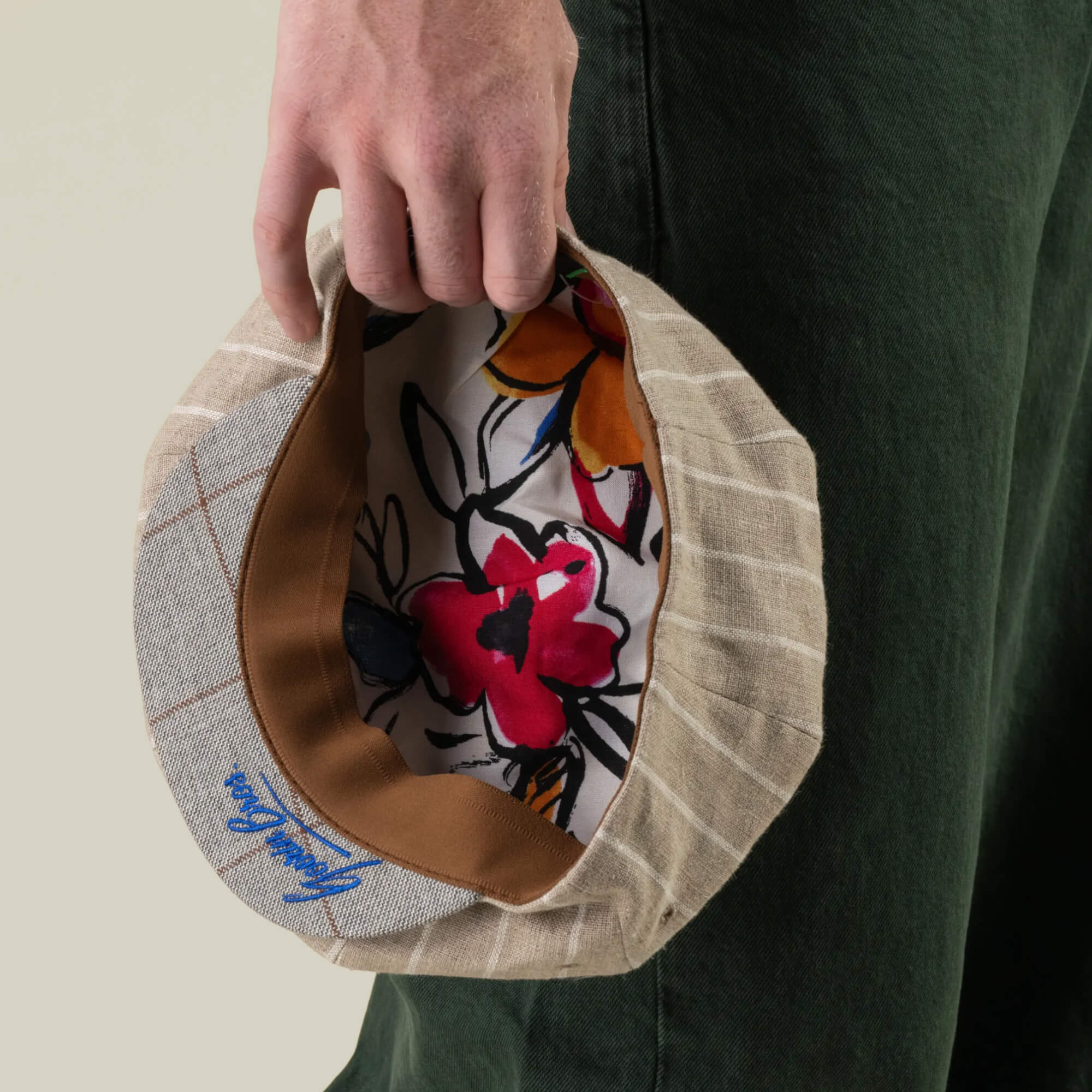 A person holds the Goorin Bros. Rincon Park hat, featuring beige pinstripes, a brown band, and a floral-patterned lining, hand cut and sewn in a Gatsby-inspired silhouette, next to green pants.