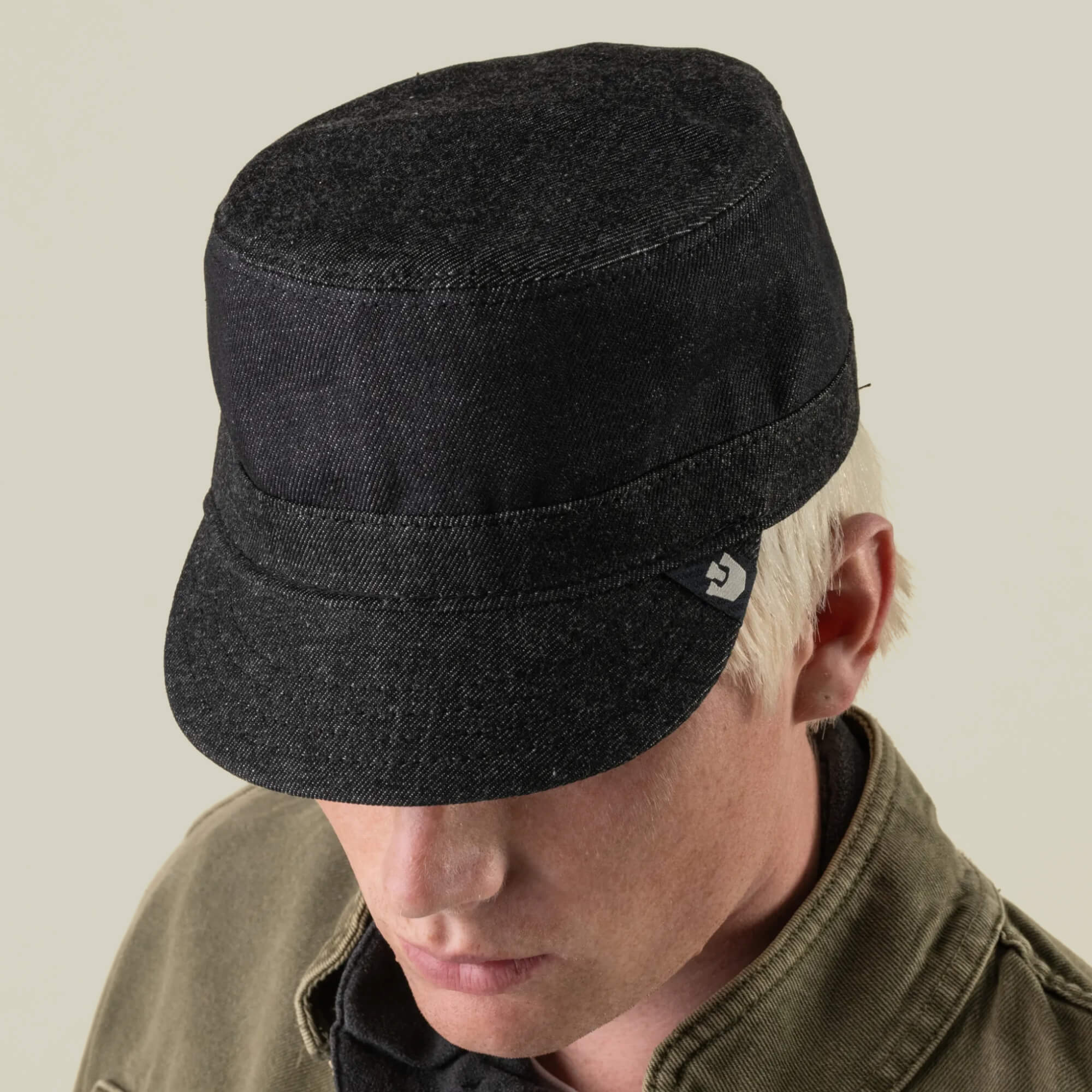 A person wearing the Goorin Bros. Devonshire dark cotton cadet cap and an olive jacket, facing downward against a neutral background. The cap is hand sewn in the USA at our New Jersey factory.