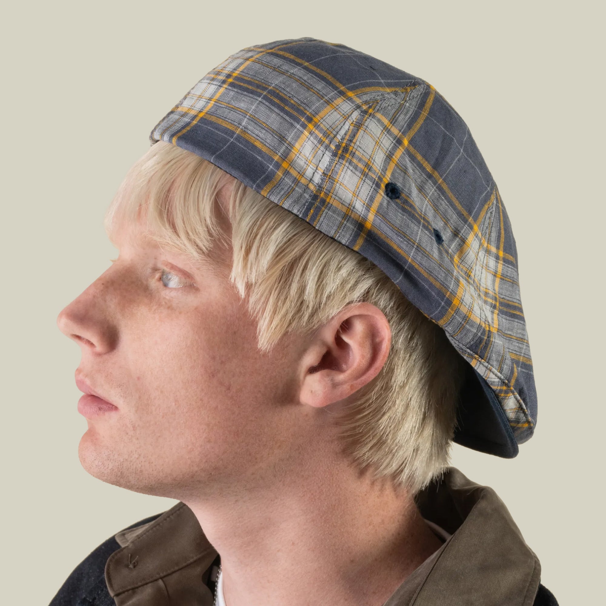Side profile of a person with blond hair wearing the Goorin Bros. Point Lobos 6 Panel Ivy hat in blue and yellow plaid, handmade in the USA from a breathable cotton blend, looking to the left against a plain light background.