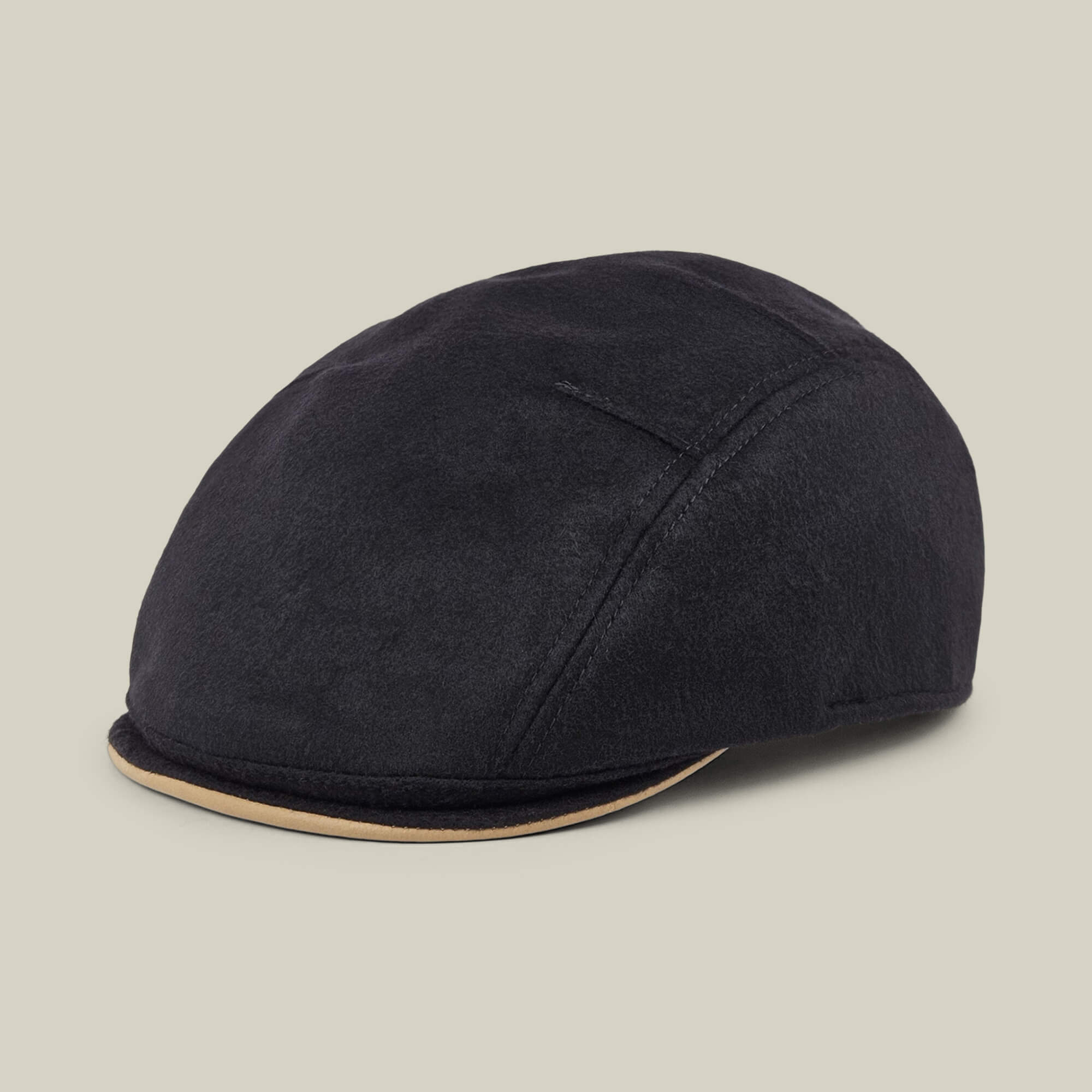 The Goorin Bros. “Cornerstone” is a classic black flat cap featuring a curved brim and subtle tan trim, handmade in New Jersey and displayed on a plain beige background.