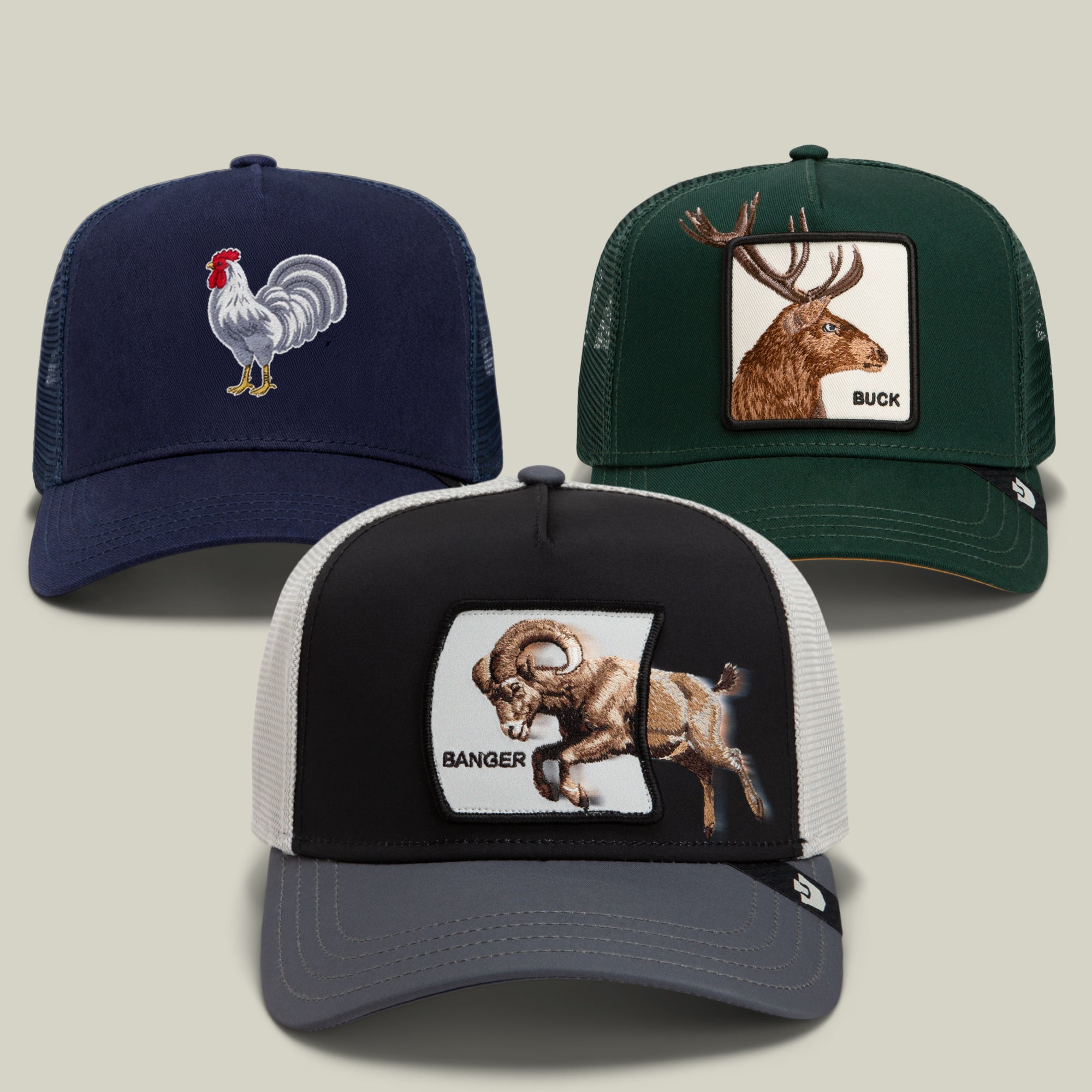 The Outside the Box Bundle by Goorin Bros. features three trucker hats with embroidered patches: a navy hat with a rooster, a green hat with a deer buck, and a black and gray hat labeled “BANGER” with a ram design, all displayed on a plain background.