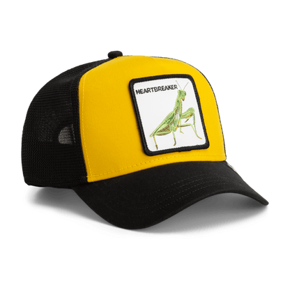 The Heartbreaker by Goorin Bros is a yellow and black trucker hat featuring a mesh back panel and an embroidered patch of a green praying mantis insect with the word Heartbreaker on the front.