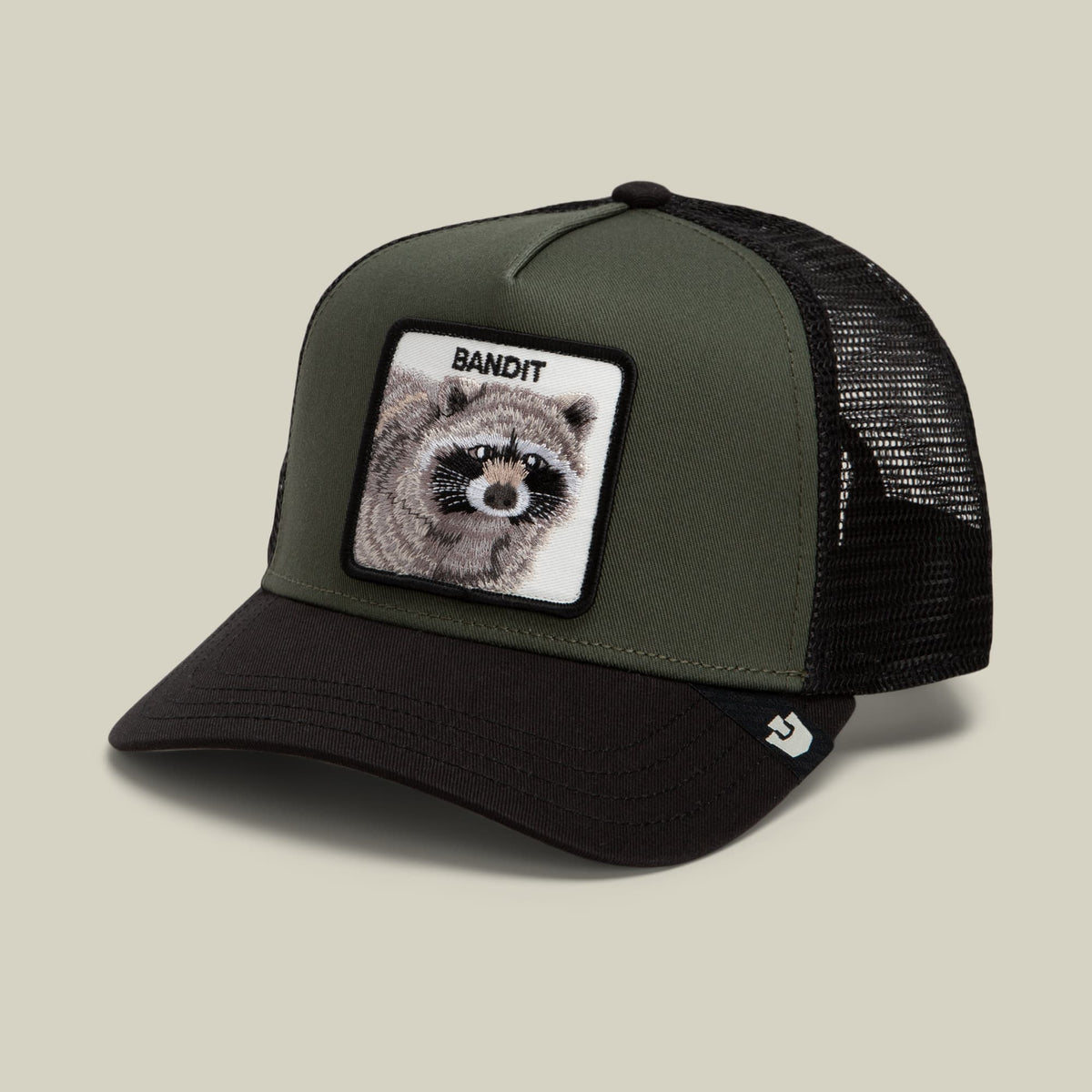 The Goorin Bros. Bandit Trucker is an olive green and black mesh trucker hat featuring an embroidered raccoon patch on the front with the word "Bandit" text above it, displayed on a neutral background.