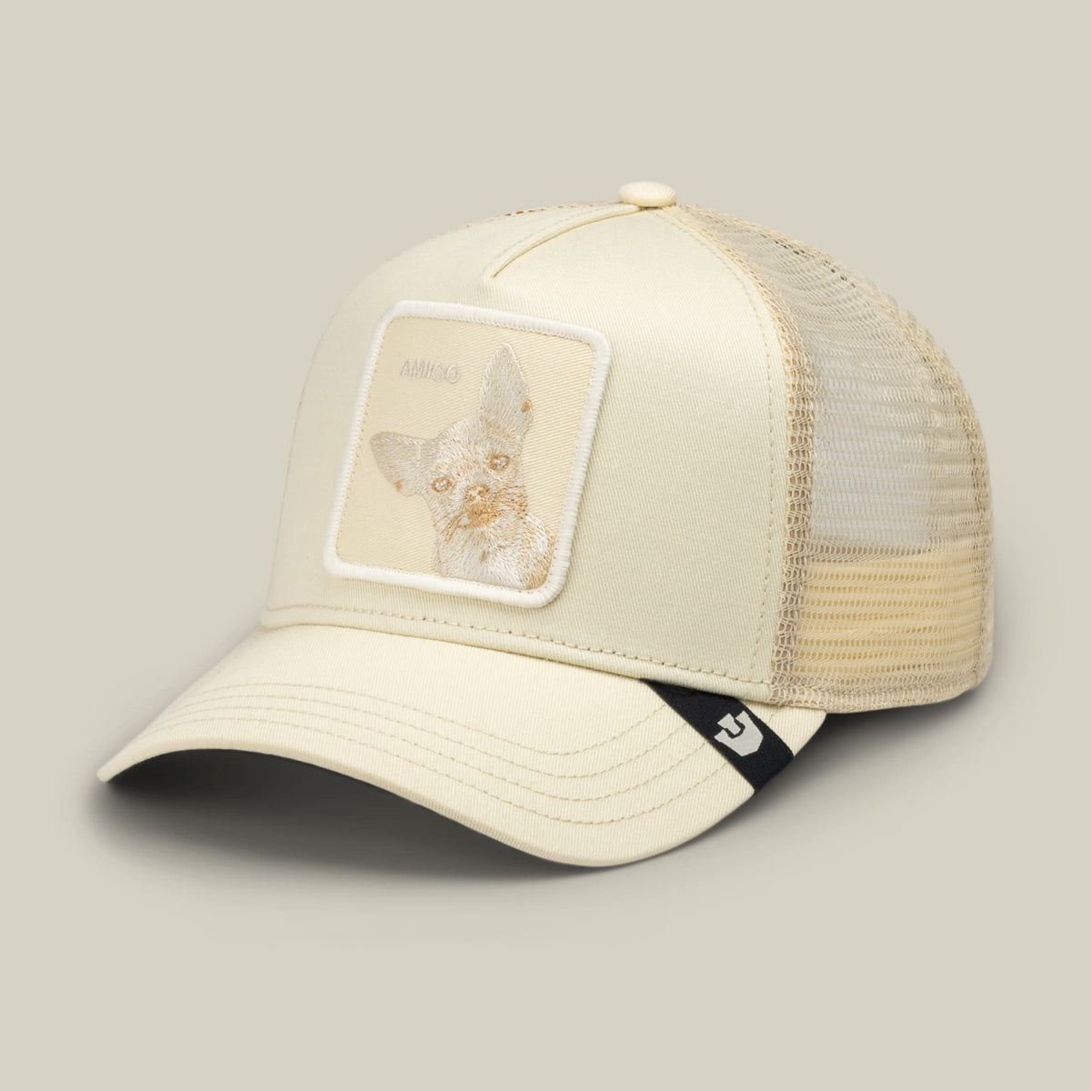 The Goorin Bros. Tonal Amigo is a cream mesh trucker hat with a structured front panel featuring a subtle animal patch and a black chin strap, shown in a studio product shot.