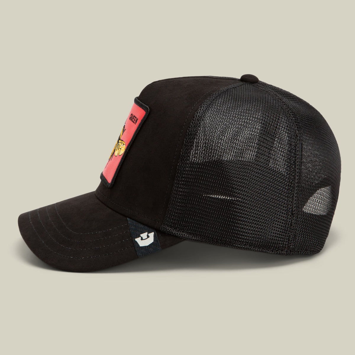 The Goorin Bros. Regina Rossa is a black trucker hat with mesh back paneling, featuring a coral pink patch with gold animal detail on the side and small brand logo on the front.