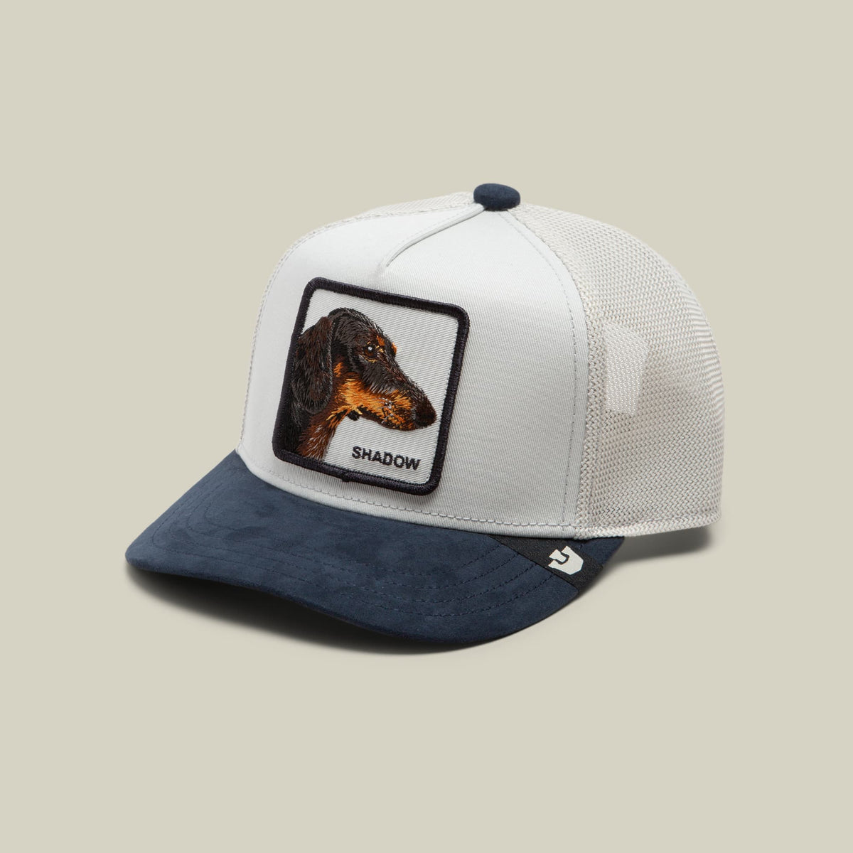 The Goorin Bros. Suede Shadow Mini is a two-tone trucker hat with a white mesh back and navy blue suede front, featuring an embroidered dachshund patch labeled "SHADOW" on the crown.