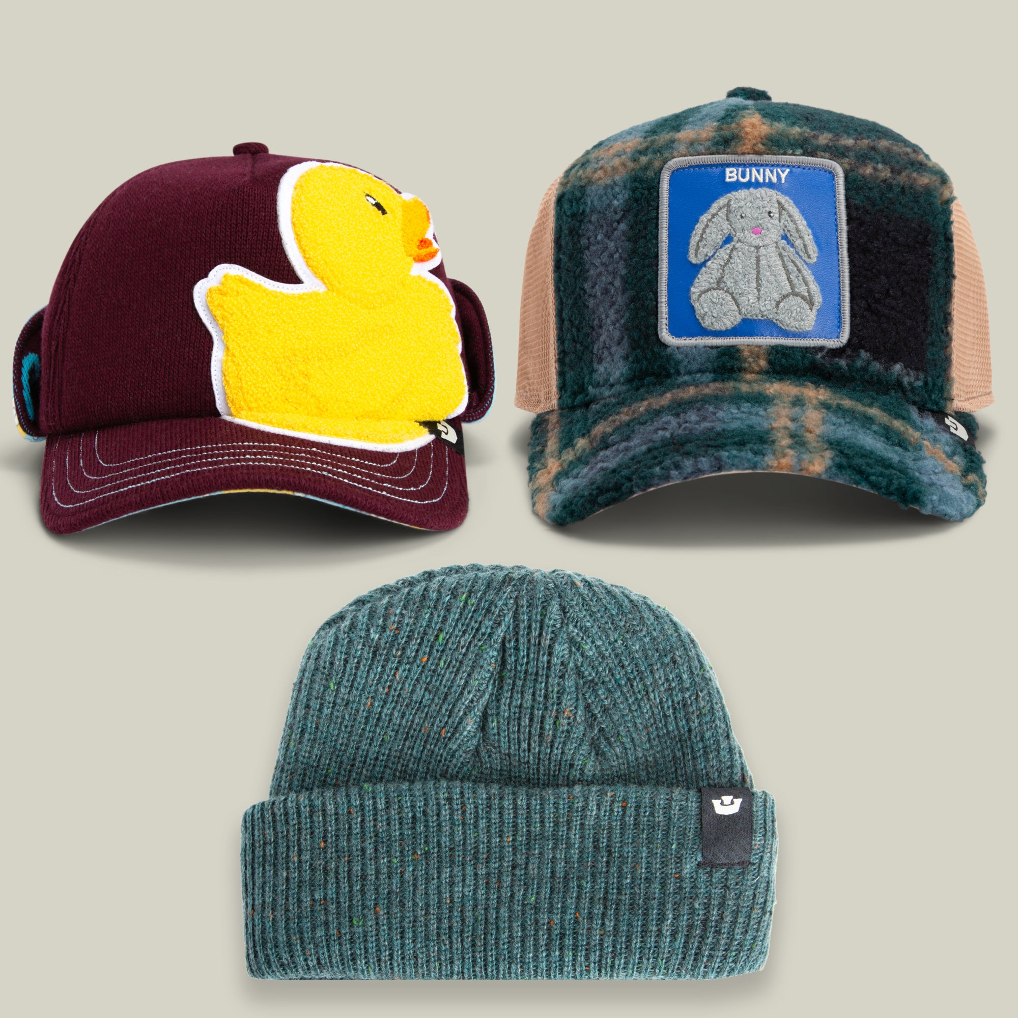 The Winter is Coming II Bundle by Goorin Bros. includes three hats: a maroon cap with a yellow rubber duck patch, a plaid trucker cap featuring a bunny patch, and a green knit beanie adorned with a small black tag.